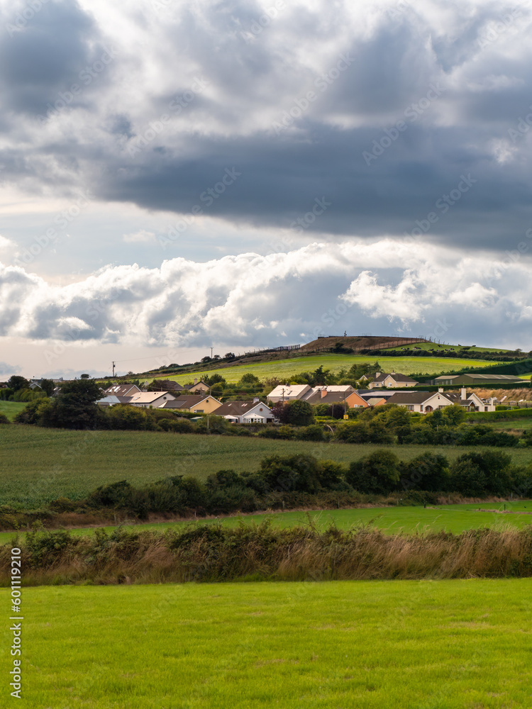 Sky with cumulus clouds over a small Irish village on a summer evening. Irish settlement in County Cork, dramatic landscape. European countryside, rustic landscape. Green grass field under clouds, sky Sky with cumulus clouds over a small Irish village on a summer evening. Irish settlement in County Cork, dramatic landscape. European countryside, rustic landscape. Green grass field under clouds, sky
