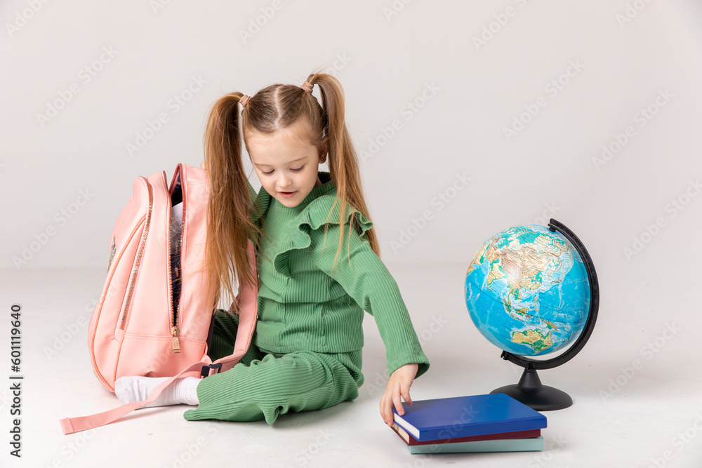 Ready for school. Full size photo of little smiling happy schoolgirl little puts textbooks in a school backpack on white background. Ready for school. Full size photo of little smiling happy schoolgirl little puts textbooks in a school backpack on white background.