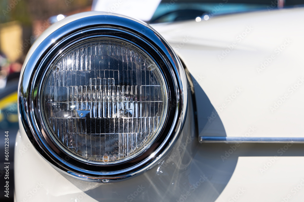 Close-up of the round headlamps of a white classic car. Beautifully restored chrome details of a historic vehicle.
