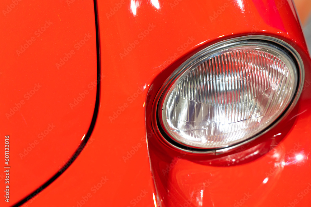 Close-up of the round headlamps of a red, sport classic car. Beautifully restored details of a historic vehicle.
