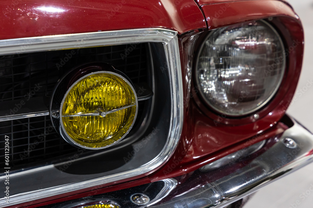 Close-up of the round headlamps of a red american classic car. Natural patine on the chrome details of a historic vehicle.
