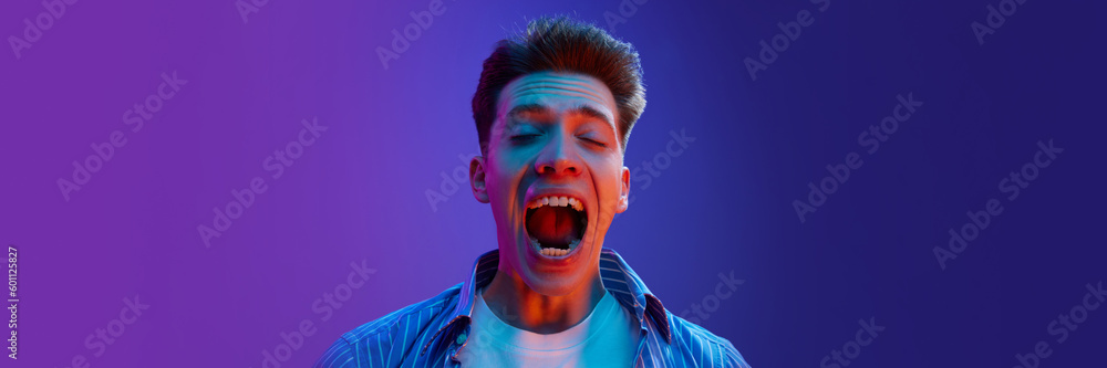Portrait of young emotive man guy in casual clothes showing success and winning look, excitement on gradient purple background in neon light. Concept of human emotions, lifestyle. Copy space for ad