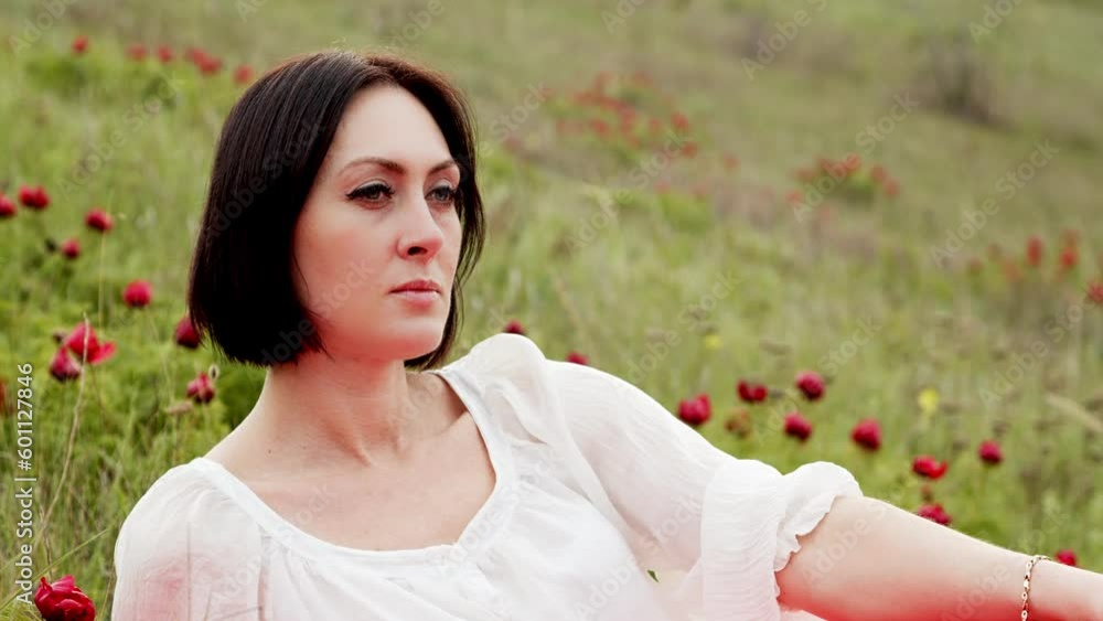 Portrait A pretty woman in a white blouse and a scarlet skirt sits in the grass among red wild peonies. Festival and holiday event Portrait A pretty woman in a white blouse and a scarlet skirt sits in the grass among red wild peonies. Festival and holiday event