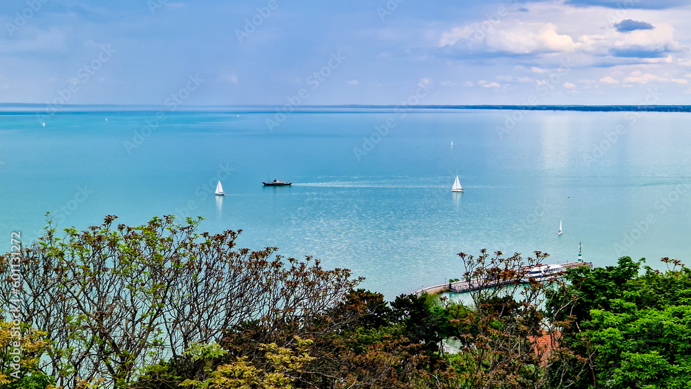 View of the clear blue water of the Lake Balaton with trees and sky with clouds. Sunny day of spring in Tihany, town of Hungary.