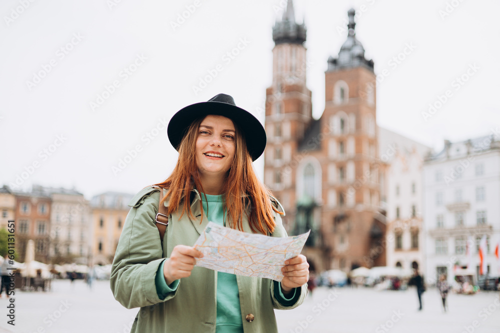 Attractive young female tourist is exploring new city. Redhead girl walking and holding a paper map in Krakow. Traveling Europe in spring. Urban lifestyle banner