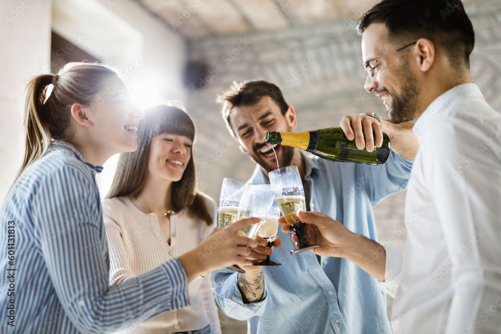 Young business colleagues pouring champagne during a party in the office. Focus is on champagne bottle Young business colleagues pouring champagne during a party in the office. Focus is on champagne bottle