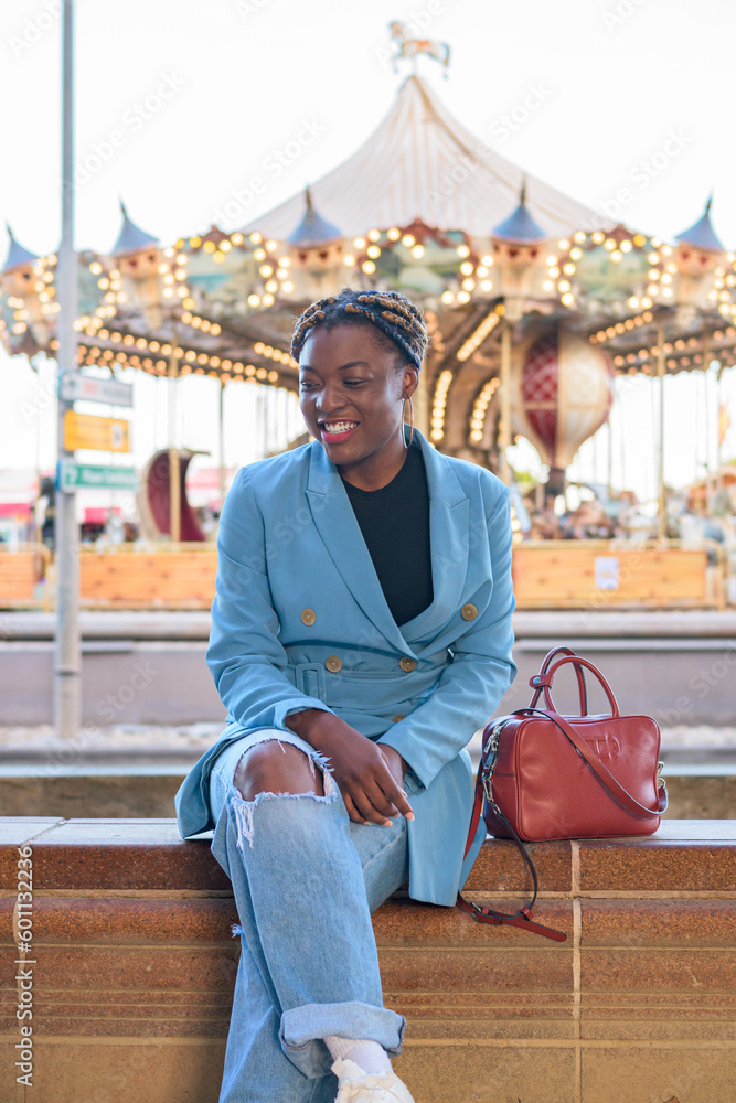 Black business woman smiles while she is sitting with a fair in the background