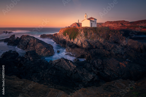 Hora dorada sobre la costa rocosa con la ermita de Virxe do Porto y el faro de Punta Frouxeira al fondo