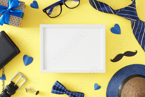 Father's Day accessories concept. Top view flat lay of modern necktie hat wallet belt bow tie glasses gift box mustache and blue hearts on light yellow background with frame for text or advert