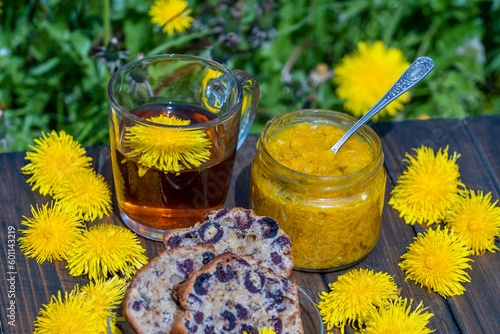 Healthy dandelion flower tea in a glass cup on the wooden table with sweet jam and cherry muffin in the spring garden, closeup