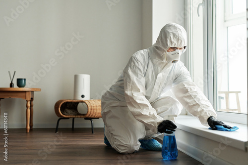 Fotografie Cleaning worker in protective suit disinfecting surface with detergent during ho