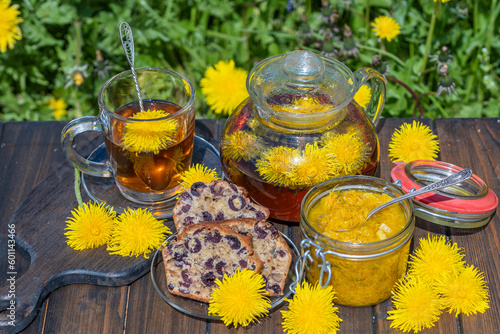 Healthy dandelion flower tea in a glass teapot on the wooden table along with sweet jam and cherry muffin in the spring garden, closeup
