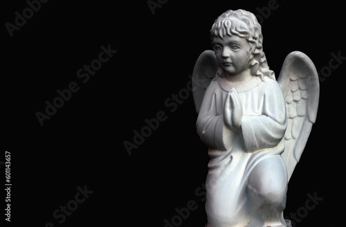Black and white image of little praying angel against dark background. Copy space.