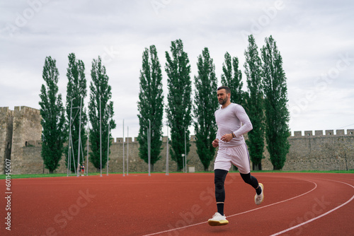 Motivated determined young male athlete running on red race track while training at sports stadium in city 