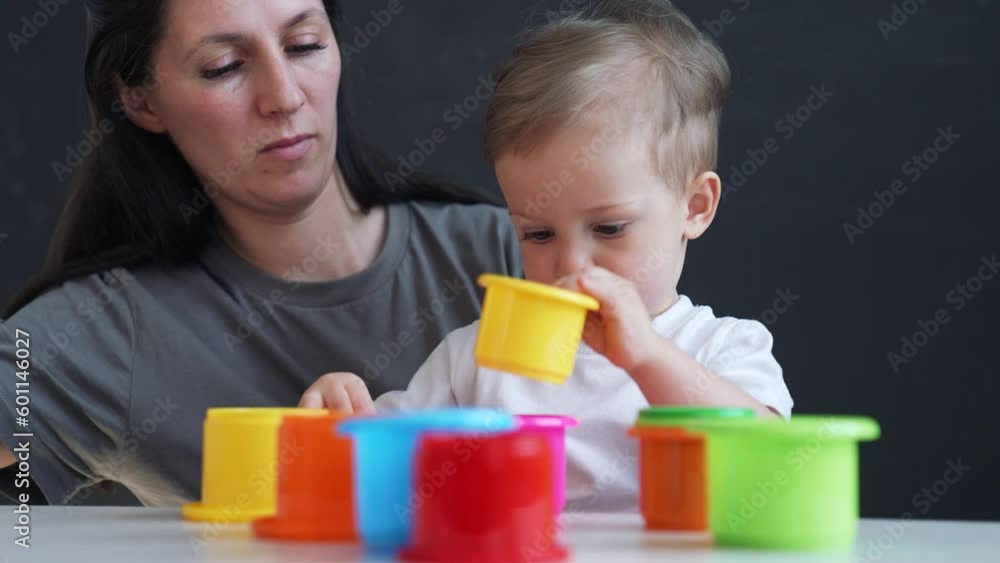Happy cute family at home. Child collects colored cubes. Mom with her baby son play with toys at home. Happy family concept. Parent helps son in learning. Preschool family education. Mom and baby play Happy cute family at home. Child collects colored cubes. Mom with her baby son play with toys at home. Happy family concept. Parent helps son in learning. Preschool family education. Mom and baby play