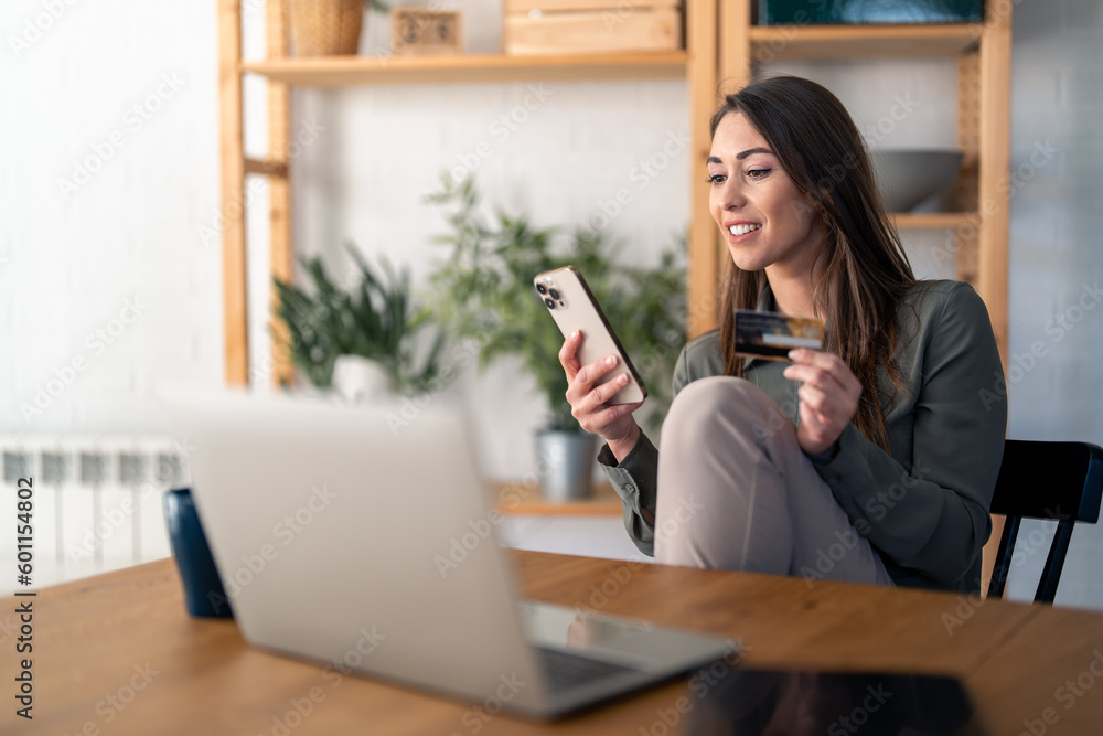 Smiling young woman looking at smart phone screen holding credit card, using mobile phone secured online e-banking app, satisfied with online cashback purchase or good electronic banking services. Smiling young woman looking at smart phone screen holding credit card, using mobile phone secured online e-banking app, satisfied with online cashback purchase or good electronic banking services.