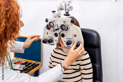 Optician and optometrist. Young woman during a visual test with phoropter. photo