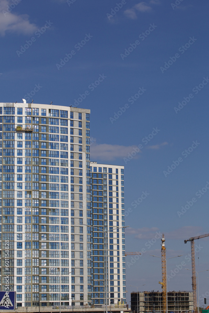 Construction site. Reinforced concrete frames of multi-storey buildings and construction cranes. Finished houses nearby. Against the background of the blue sky. Construction site. Reinforced concrete frames of multi-storey buildings and construction cranes. Finished houses nearby. Against the background of the blue sky.