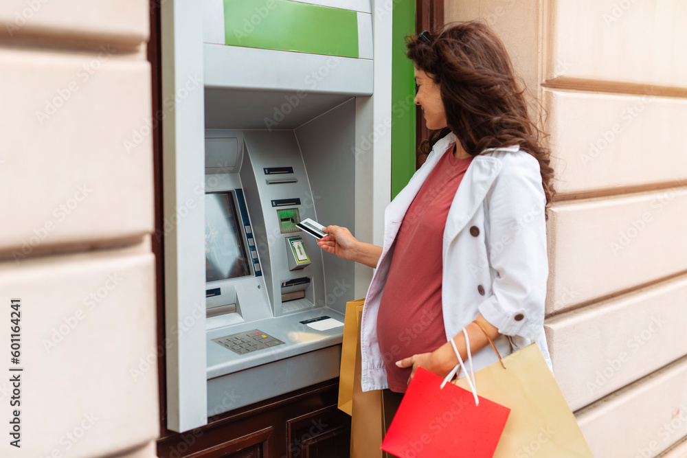 Woman standing in front of ATM machine, smiling and holding credit or debit card Woman standing in front of ATM machine, smiling and holding credit or debit card