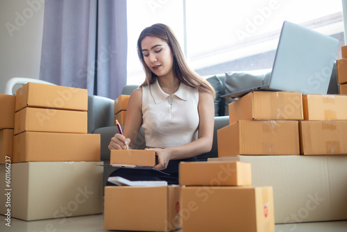 woman checking package of goods from customer online order is alone in her home office as she is an SME entrepreneur and uses her phone and tablet to market online. concept online sales business © thatinchan