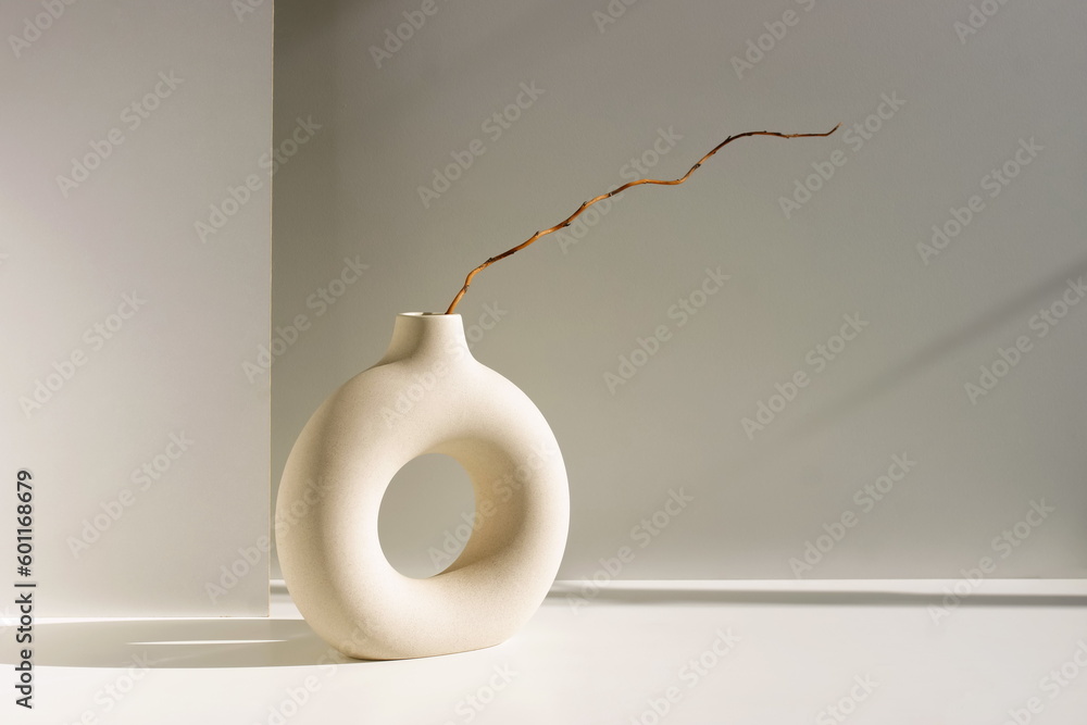 Modern beige ceramic vase  with branch and sunlight shadow on white table near gray wall.Copy space, Minimal Scandinavian interior accessories.  - obrazy, fototapety, plakaty 