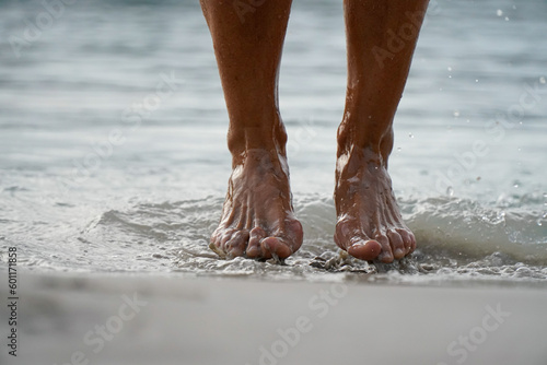 Fotografi the barefooted feet of a woman splashing on the shore of the beach