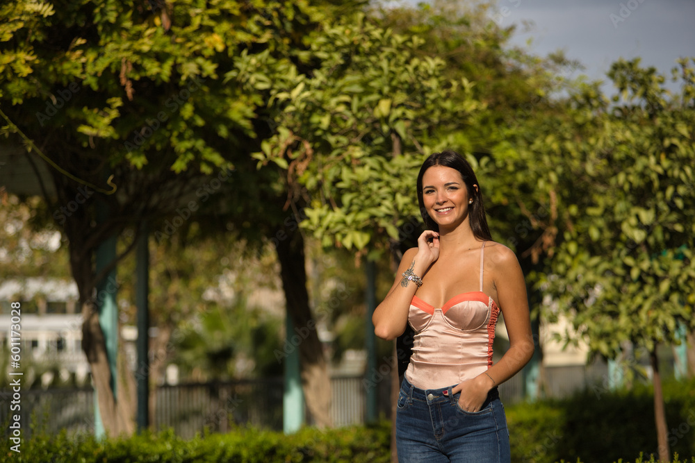 Young and beautiful woman with straight brown hair, orange top, jeans and jacket over her shoulder, looking at the camera smiling and happy. Concept fashion, beauty, trend, relax, millennial. Young and beautiful woman with straight brown hair, orange top, jeans and jacket over her shoulder, looking at the camera smiling and happy. Concept fashion, beauty, trend, relax, millennial.
