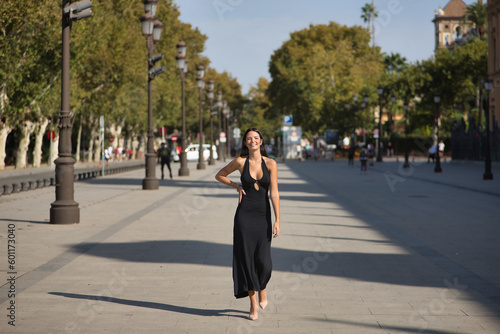 Young and beautiful woman with straight brown hair, wearing an elegant black dress, walking downtown, empowered and independent, smiling and happy. Concept fashion, beauty, empowerment, millennial.