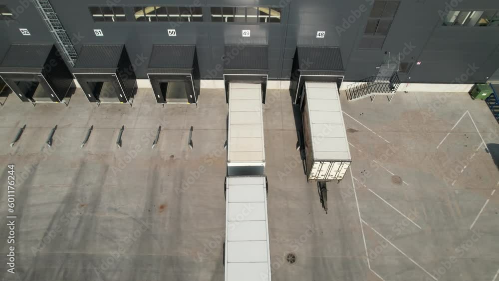 Aerial circling view of a logistics center with warehouse, loading hub with many semi-trailers trucks load/unload goods Aerial circling view of a logistics center with warehouse, loading hub with many semi-trailers trucks load/unload goods