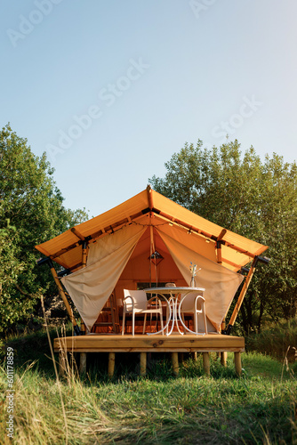 Cozy open glamping tent with light inside during sunset. Luxury camping tent for outdoor summer holiday and vacation. Lifestyle concept