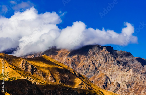 Rocky slopes of Caucasus mountains in autumn colours, clouds cover peaks. photo