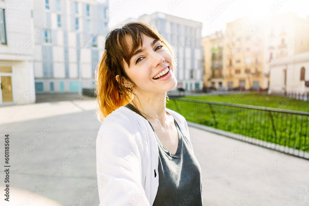 Closeup portrait of young beautiful woman smiling outdoors. Front view of happy girl with toothy smile looking at camera standing over city background.