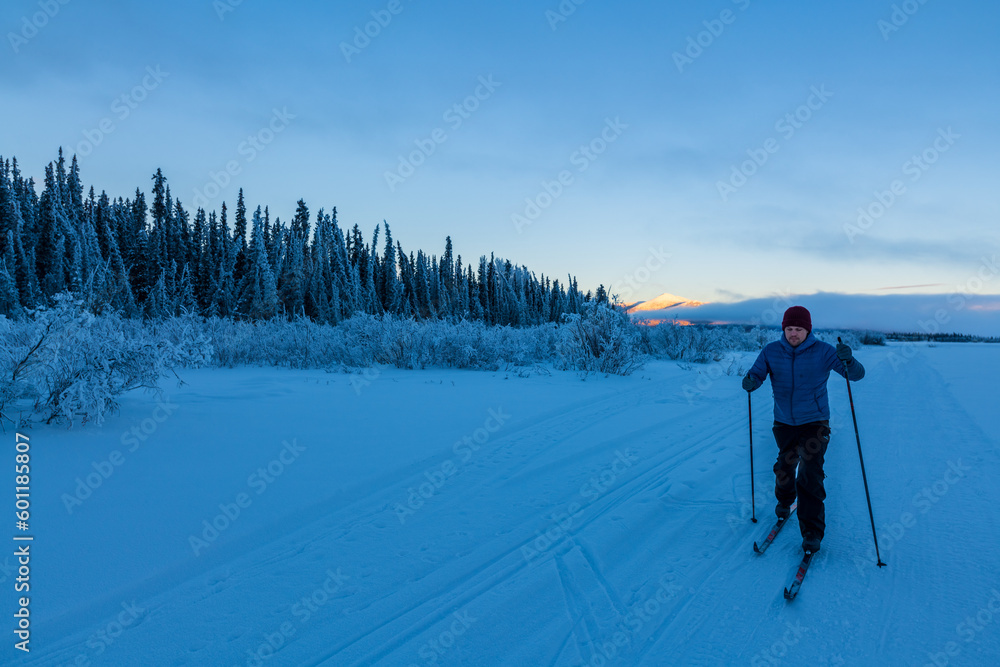 One person skiing along the frozen Yukon River in winter season with stunning blue hour scenery at sunset in the background and frosty landscape. 