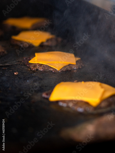 cooking burgers with cheddar cheese on a griddle in fast food restaurant