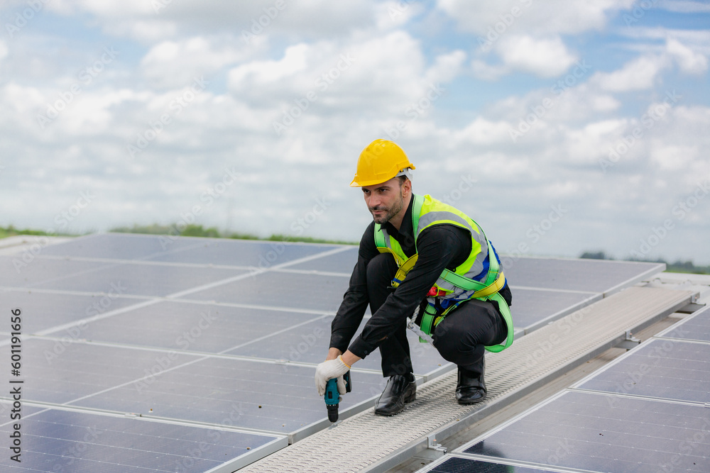 Handsome young male engineer wearing safety vest and jacket with gloves and tools along with hard hat helmet standing on solar panel while checking and looking at its maintenance Handsome young male engineer wearing safety vest and jacket with gloves and tools along with hard hat helmet standing on solar panel while checking and looking at its maintenance