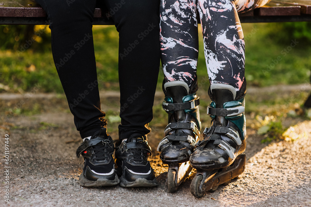 Two girlfriends, girls are sitting on a park bench in roller skates and sneakers, preparing for sports skating. Photography, portrait, sport, lifestyle.