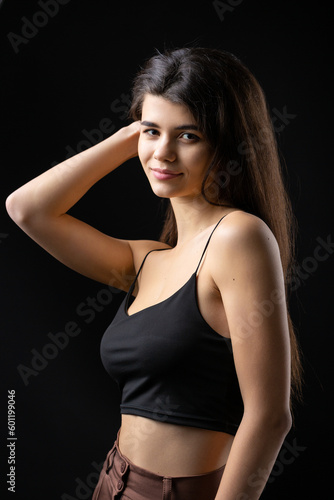 Classic studio portrait of a young brunette dressed in a black top, who is sitting on a chair against a black background. © Budjak Studio