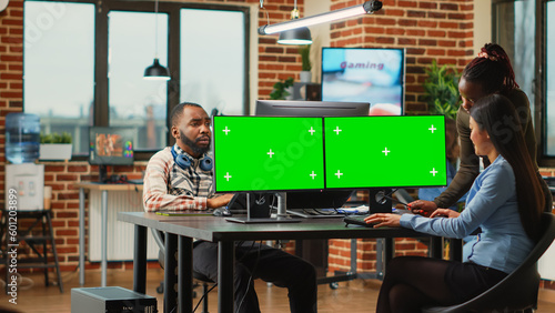 Diverse team of female employees analyzing computers with greenscreen template, women looking at mockup display. Content creators using isolated chroma key with blank copyspace on monitors.