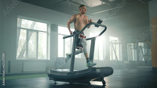 Full shot of athletic young man with sweaty naked torso running fast on treadmill in spacious empty gym. Sportsman kick his legs high, hands move fast. High quality 4k footage
