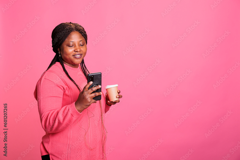 Beautiful young adult drinking coffee while enjoying free time in studio browsing on internet, searching funny video on phone while posing in studio. Excited woman posting selfie on social media Beautiful young adult drinking coffee while enjoying free time in studio browsing on internet, searching funny video on phone while posing in studio. Excited woman posting selfie on social media