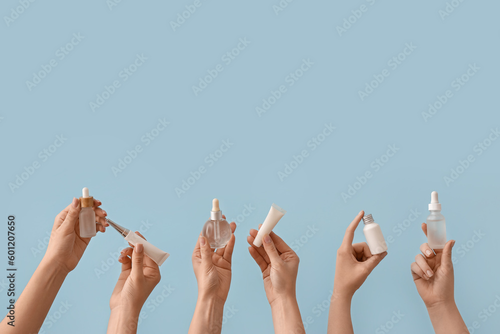 Hands holding different cosmetic products on light blue background - obrazy, fototapety, plakaty 