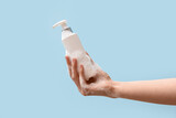 Hand holding bottle of shampoo on light blue background