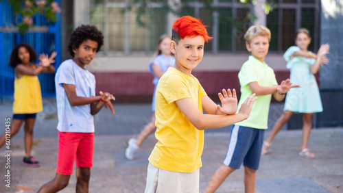 Foto Smiling boy with dyed hair dancing with team outdoors and having fun