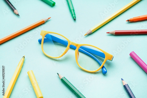Stylish yellow eyeglasses with colorful pencils on pale turquoise background