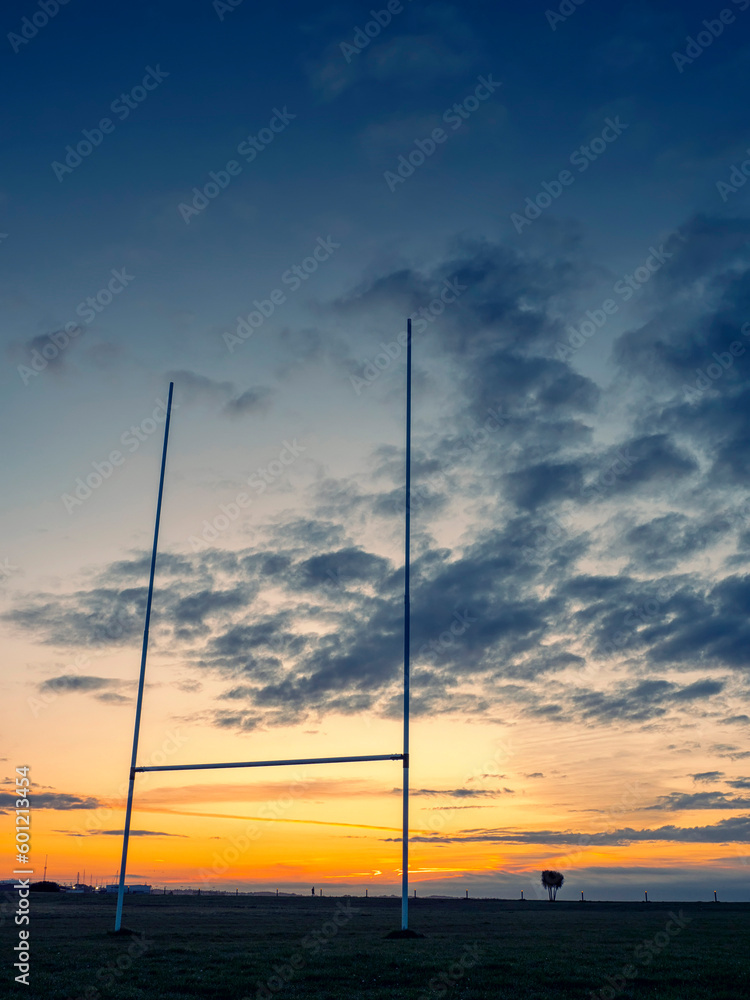 Silhouette of a tall goal post for Irish National sports comogie, hurling, rugby and gaelic football against blue and orange sun rise sky.