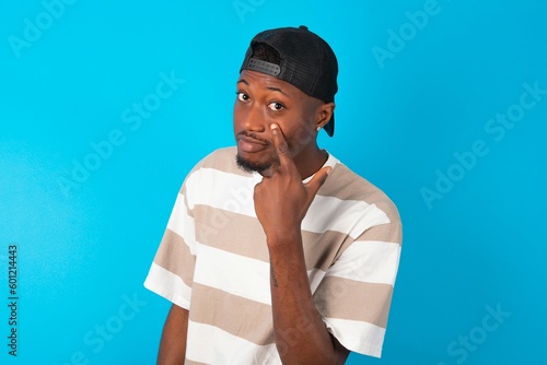 Handsome man wearing striped t-shirt and cap over blue background  Pointing to the eye watching you gesture, suspicious expression. photo