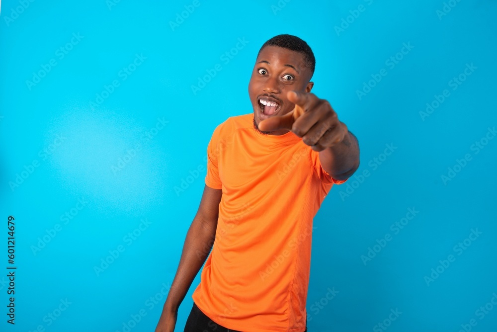 Handsome man wearing orange T-shirt over blue background pointing displeased and frustrated to the camera, angry and furious ready to fight with you. Handsome man wearing orange T-shirt over blue background pointing displeased and frustrated to the camera, angry and furious ready to fight with you.