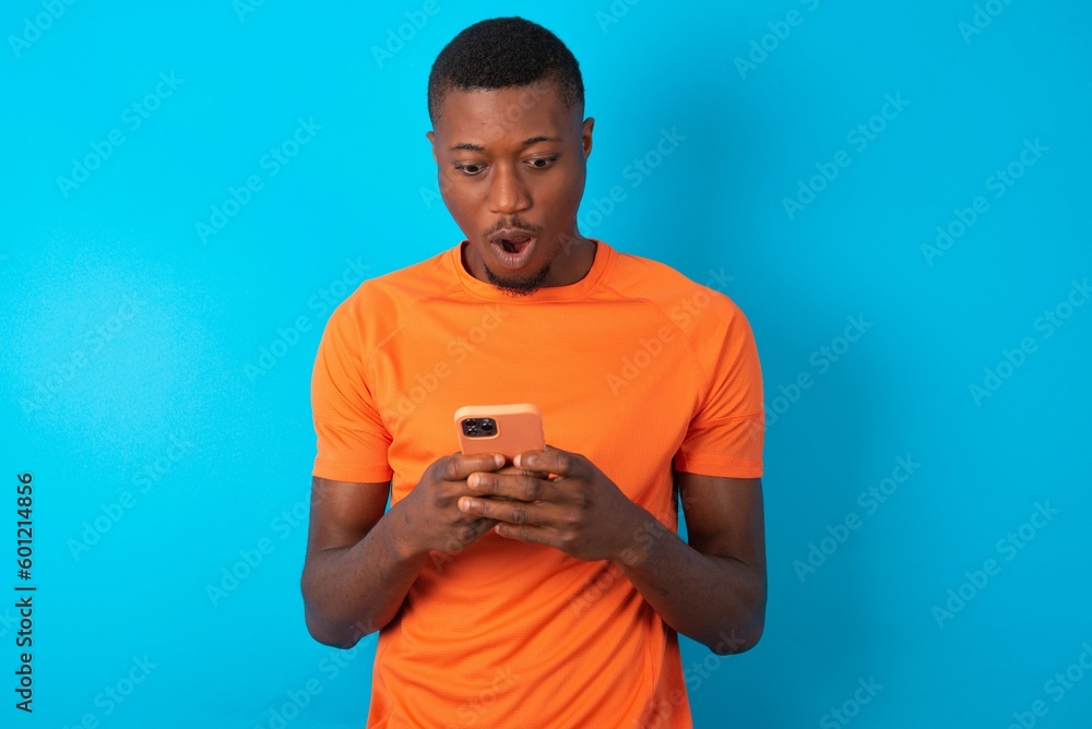 Handsome man wearing orange T-shirt over blue background using mobile phone chatting free time . Handsome man wearing orange T-shirt over blue background using mobile phone chatting free time .