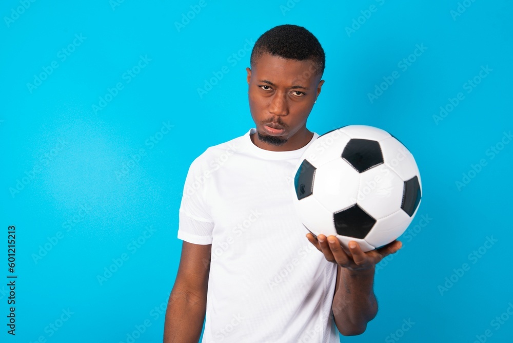 Man wearing white T-shirt holding a ball over blue background depressed and worry for distress, crying angry and afraid. Sad expression. Man wearing white T-shirt holding a ball over blue background depressed and worry for distress, crying angry and afraid. Sad expression.