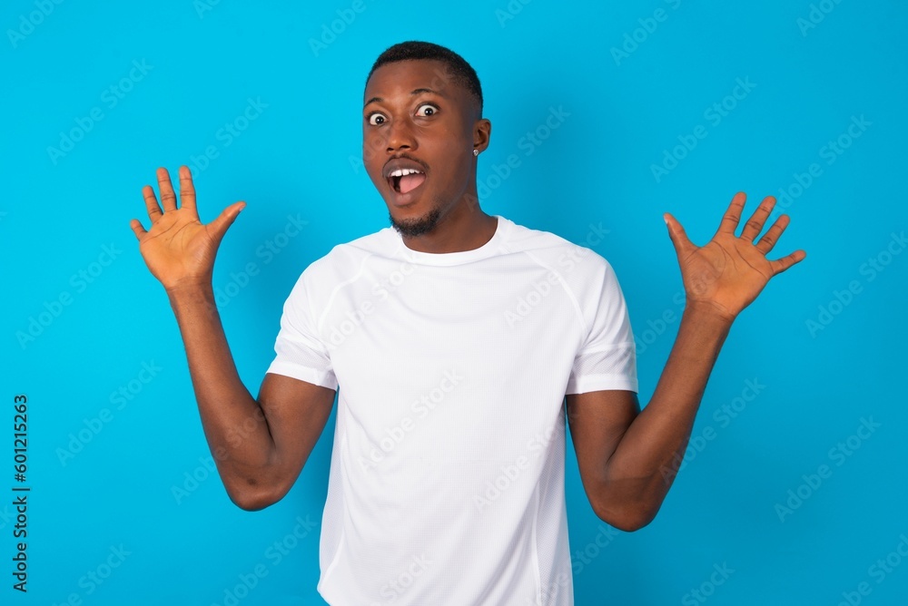 Delighted positive Handsome man wearing white T-shirt over blue background opens mouth and arms palms up after having great result Delighted positive Handsome man wearing white T-shirt over blue background opens mouth and arms palms up after having great result